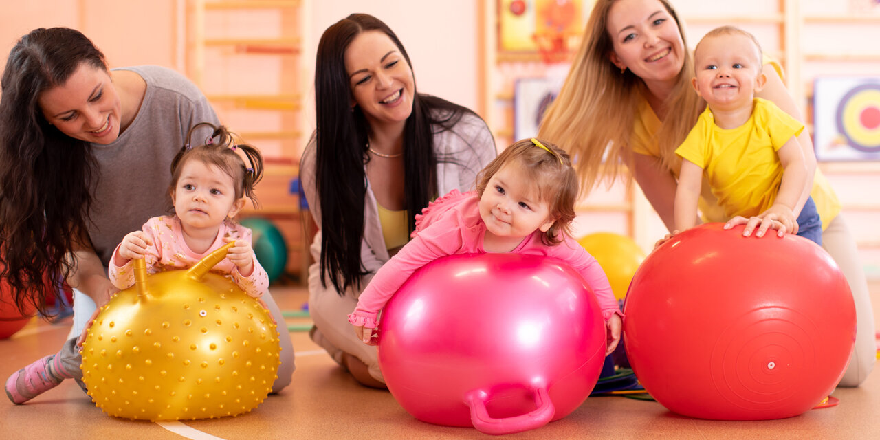 AdobeStock_304693426 Gruppe von Müttern und ihren Kindern, die auf Gymnastikbällen im Fitnessstudio Yogaübungen machen