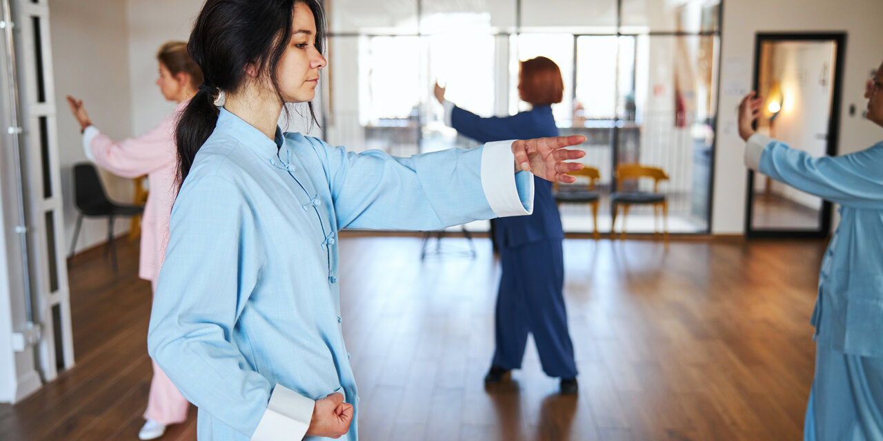 AdobeStock_439648229 Eine Gruppe von Menschen in chinesischer Kleidung, die während der Qigong-Übung langsame Bewegungen mit rhythmischer Atmung kombinieren.