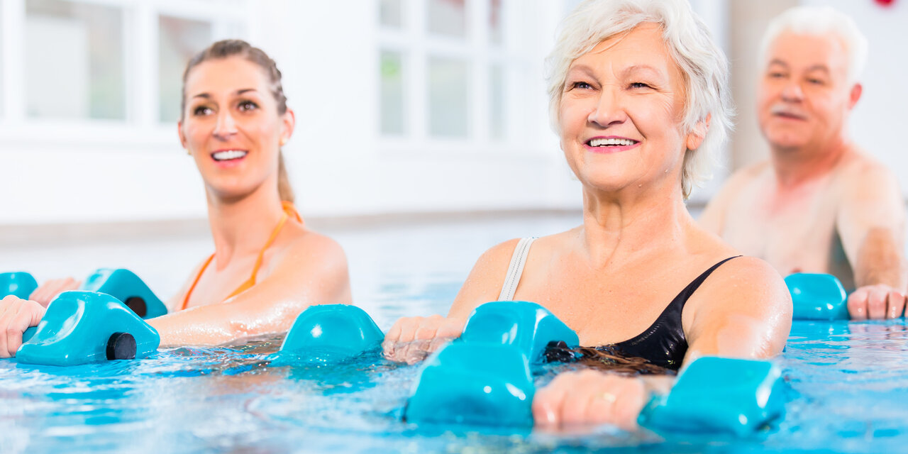 AdobeStock_190246283 Junge und ältere Menschen bei Wassergymnastik-Physiotherapie mit Hanteln.