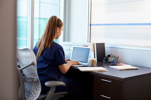 Stock-Fotografie-ID:629600102 - Nurse Wearing Scrubs Working At Desk In Office – Stockfoto